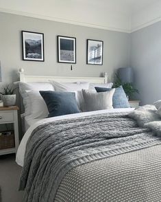 a bed with pillows and blankets on top of it in a bedroom next to two framed pictures