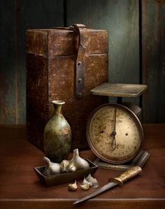 an old suitcase, clock and garlic on a table next to it is still life