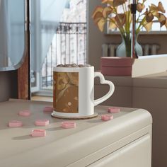 a coffee mug with pink marshmallows sitting on top of a white dresser