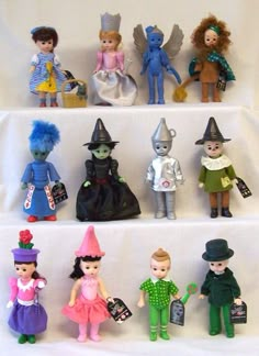 there are many small toy dolls on the shelf in front of each other, all wearing different outfits and hats