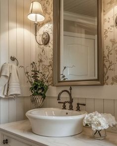 a bathroom sink sitting under a mirror next to a white counter top with flowers on it