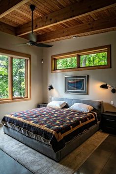 a bed sitting under two windows in a bedroom next to a window sill and ceiling fan