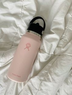 a pink water bottle sitting on top of a white bed covered in sheets and pillows