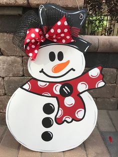 a snowman with a red bow and polka dots on it's head is standing in front of a brick wall