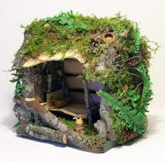 a miniature house made out of wood and moss covered walls, with plants growing on the roof