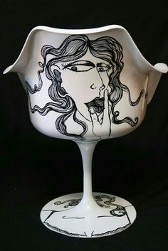 a white vase with black designs on the bottom and sides, holding a woman's face