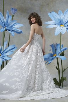 a woman standing in front of blue flowers wearing a white wedding dress and posing for the camera