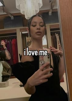 a woman looking at her cell phone in front of a mirror that says i love me