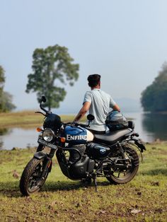 a man sitting on top of a motorcycle next to a body of water and trees