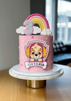 a pink birthday cake with a dog on top and a rainbow in the middle is sitting on a table