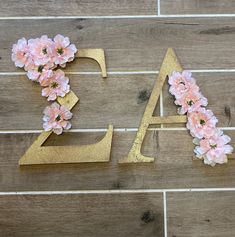 the letters are made out of gold and pink flowers on a wood floor with a brick wall in the background