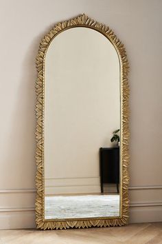 a large gold mirror sitting on top of a hard wood floor next to a wall