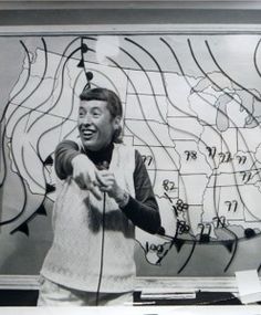 a man standing in front of a map holding a microphone and pointing at something on the wall