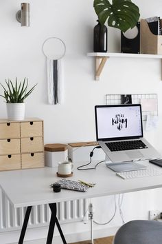 a laptop computer sitting on top of a white desk next to a potted plant