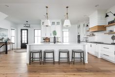 a large kitchen with white cabinets and wooden floors, two stools at the island