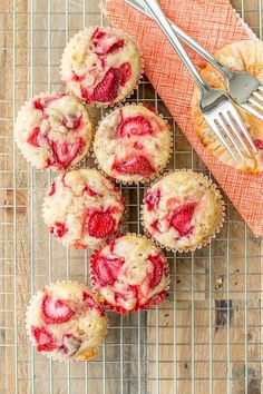 several strawberry muffins on a cooling rack with a fork and cupcake in the background