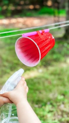 a hand holding a red and white plastic cup on a clothes line with trees in the background