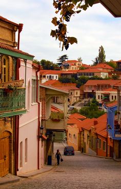 a person is walking down the street in front of some buildings and trees with red roofs