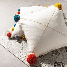 two white pillows with colorful pom - poms on them sitting on a patterned area rug