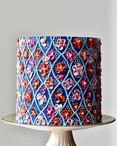 a blue and red cake with flowers on it sitting on a table next to a white wall