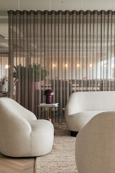 a living room with two white chairs and a round glass table in front of sheer curtains