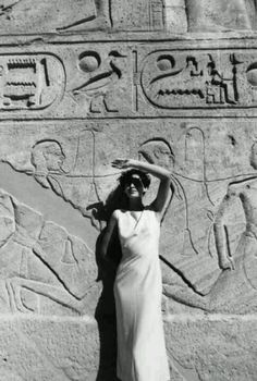 a woman standing in front of a wall with egyptian writing on it's side