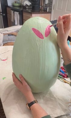 a woman is painting an easter egg with pink paint on the outside and green inside