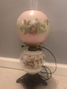 a pink lamp with flowers on it sitting on a stand in front of a wall