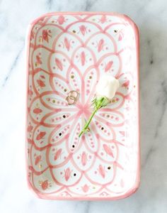 a pink and white tray with a single rose on it, sitting on a marble surface