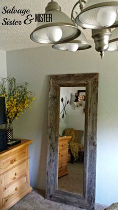 a mirror sitting on top of a wooden dresser next to a lamp shade and window