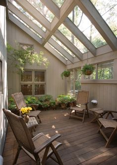 a wooden deck with chairs and potted plants on the top floor, under a glass roof