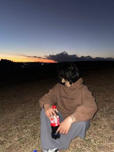 a person sitting on the ground with a bottle in their hand and a sky background