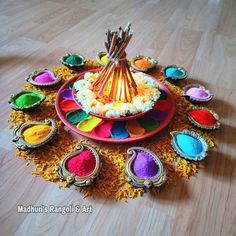 an assortment of colorful powders on a plate with incense sticks and spoons in the center