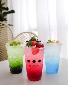 three different colored drinks on a table with strawberries and blueberries in the cups