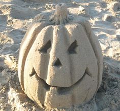 a sand pumpkin sitting in the sand with its face carved into it's head