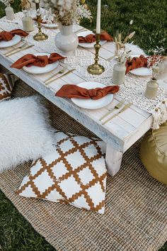 a table set up with candles, plates and napkins for dinner on the grass