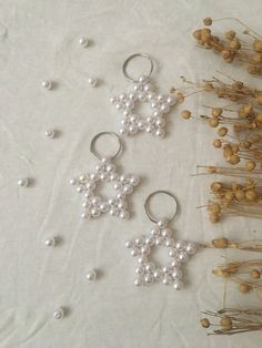 three pairs of earrings with pearls on them sitting next to some dried grass and flowers