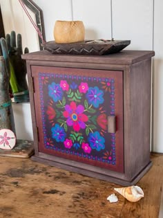 an old wooden cabinet painted with colorful flowers and shells on the table next to it