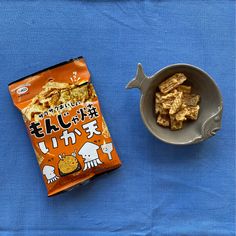 a bowl of cereal next to a bag of crackers on a blue table cloth