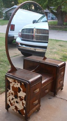 an old dresser and mirror are sitting on the sidewalk in front of a parked car