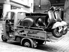 an old photo of a scooter on the back of a truck parked in front of a building