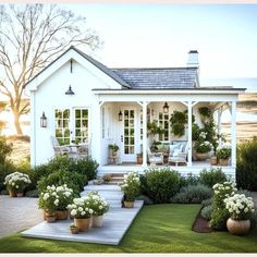 a small white house with potted plants and flowers on the front lawn, next to a deck