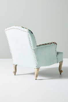 a white chair with wooden legs and studded trimmings on the arm rest