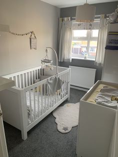 a baby's room with a white crib and grey carpeted flooring