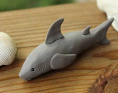 a toy shark laying on top of a wooden table next to two seashells