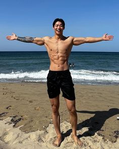 a man standing on top of a sandy beach next to the ocean with his arms outstretched