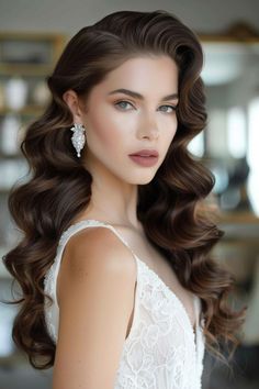 a woman with long brown hair wearing a white dress and pearls in her hair is looking at the camera