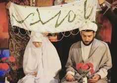 two men dressed in traditional garb sitting next to each other with flowers on their heads