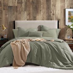 a bed with green sheets and pillows in front of a wooden wall