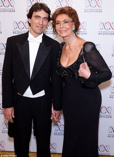 two people standing next to each other on a red carpet at an awards event, one in a tuxedo and the other in a black dress